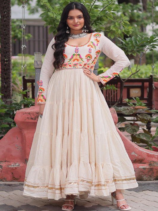 Woman in a traditional outfit with intricate patterns standing outdoors.