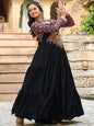 Woman in a black traditional outfit with floral patterns standing outdoors.