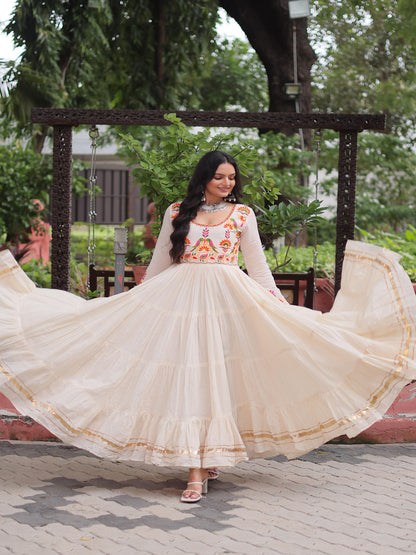 Woman in a traditional outfit with a floral top and beige skirt, standing outdoors.