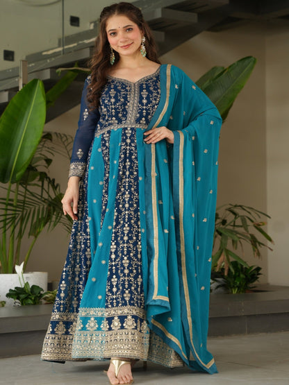 Woman in a blue and navy traditional outfit standing indoors with plants in the background