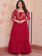 Woman wearing a red traditional outfit with intricate designs against a decorative wall.