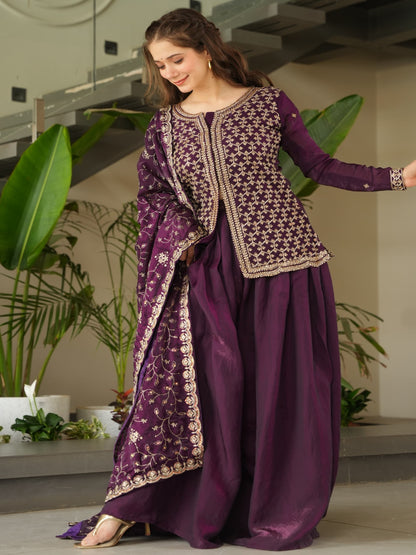 Woman in a purple traditional outfit standing in a modern indoor setting with plants.