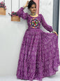 Woman wearing a purple traditional outfit with a colorful design, standing indoors.