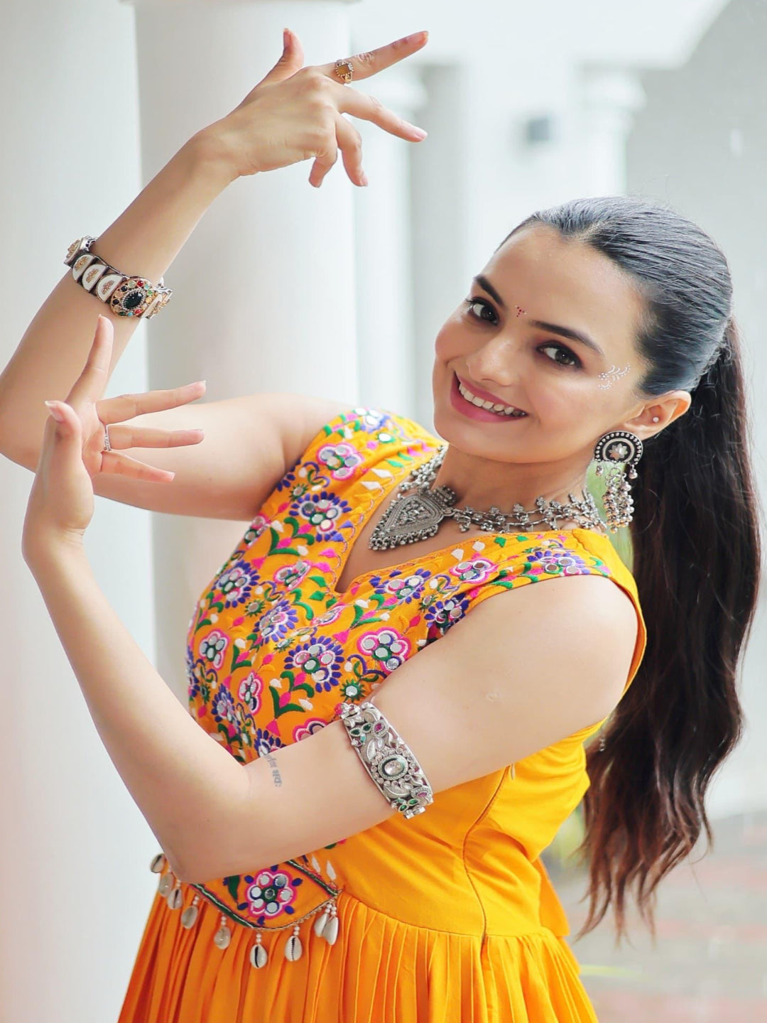 Woman in a bright yellow traditional outfit with floral patterns, posing indoors.