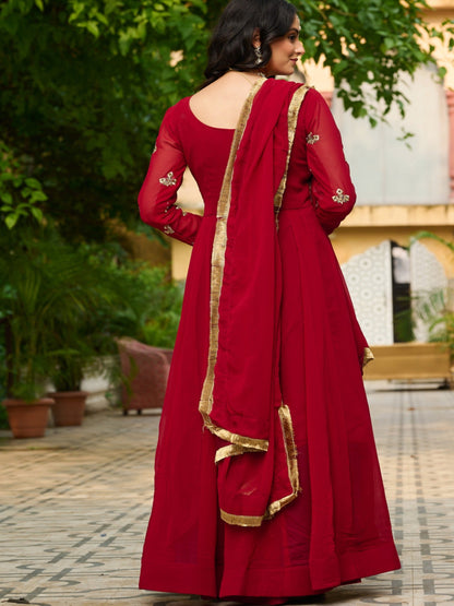 Woman in a red traditional outfit with gold details standing outdoors.