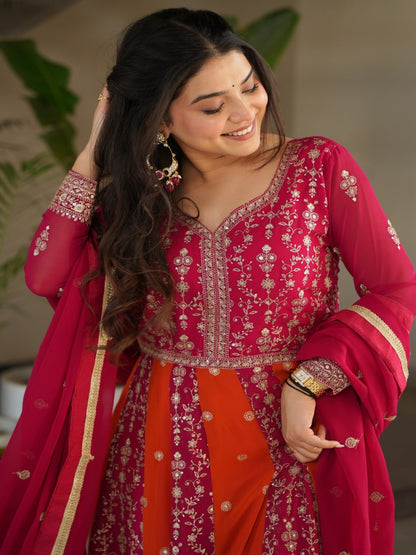 Woman in a traditional pink and red outfit with intricate designs, standing indoors.