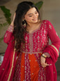 Woman in a traditional pink and red outfit with intricate designs, standing indoors.