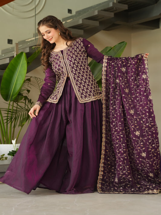 Woman in a purple traditional outfit with a matching dupatta, standing indoors.
