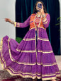 Person wearing a purple traditional outfit with gold details in front of a dark archway.