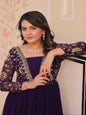 Woman wearing a purple dress with floral embroidery indoors.