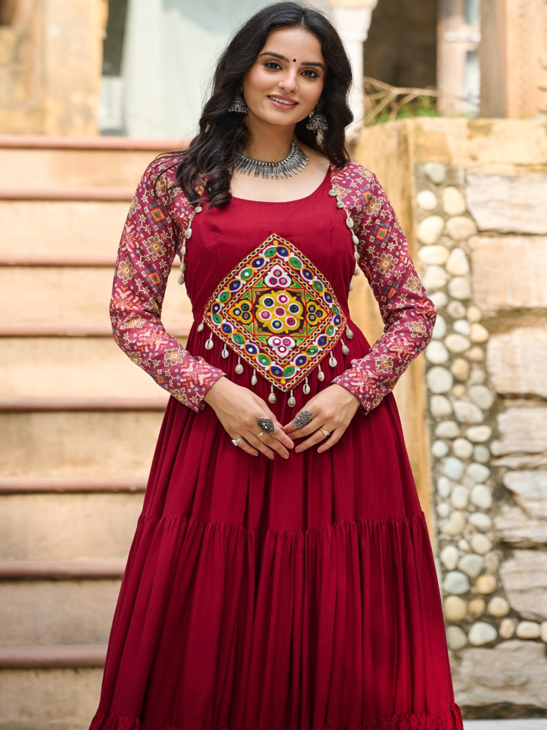 Woman in a red traditional outfit with floral patterns standing outdoors.