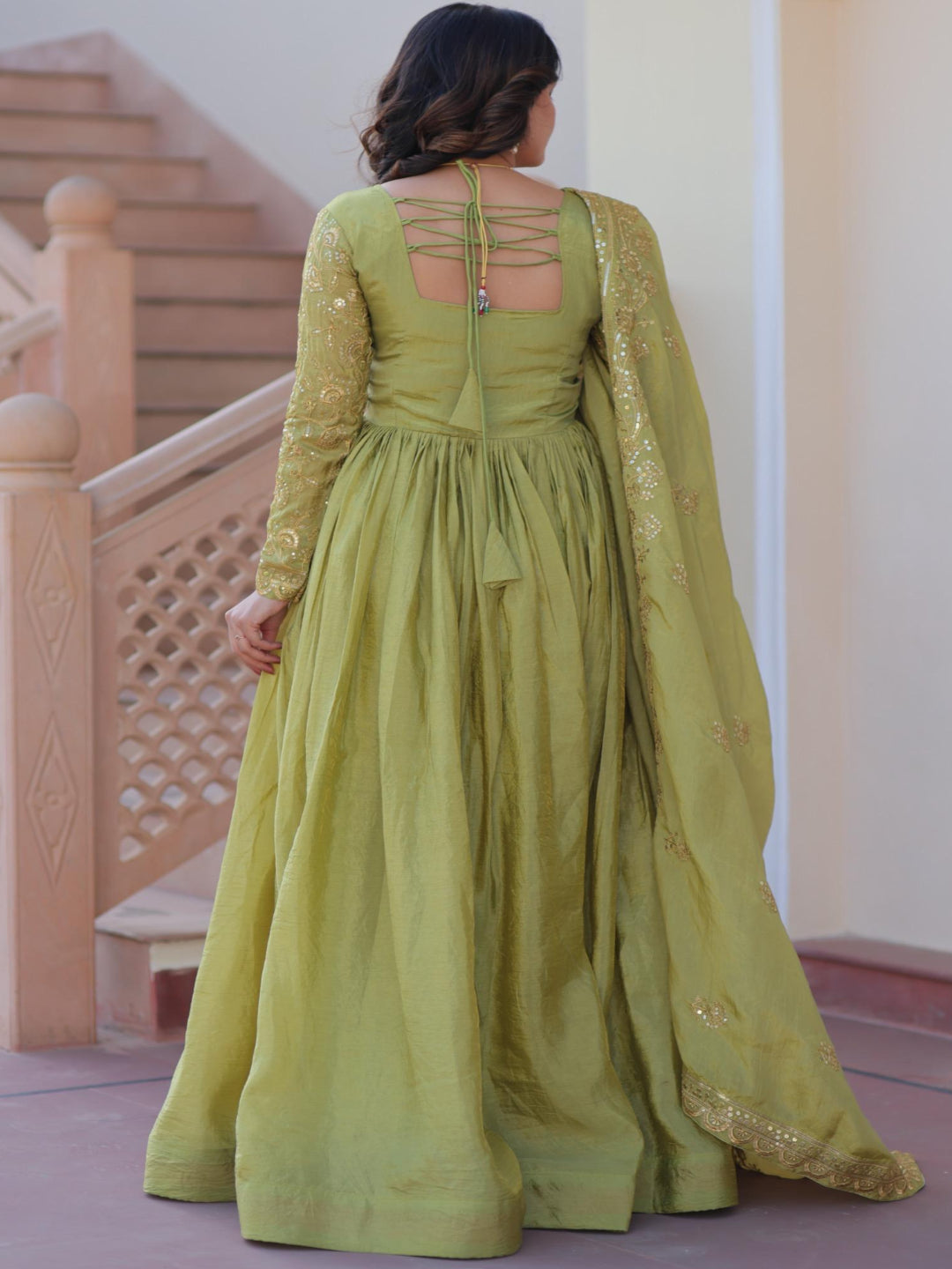 Woman wearing a green dress with intricate detailing in an indoor setting.