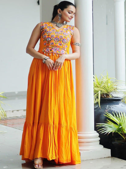 Woman in an orange and patterned dress standing in a white architectural setting with columns and plants.