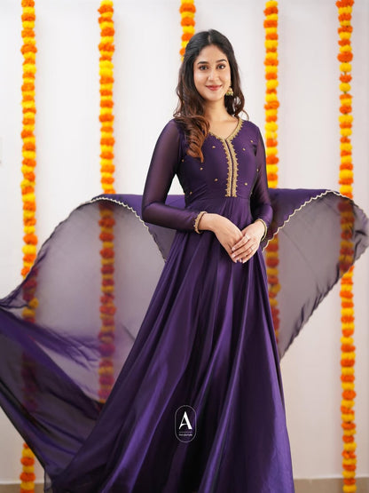 Woman in a purple dress standing against a decorated background with orange and yellow flowers.