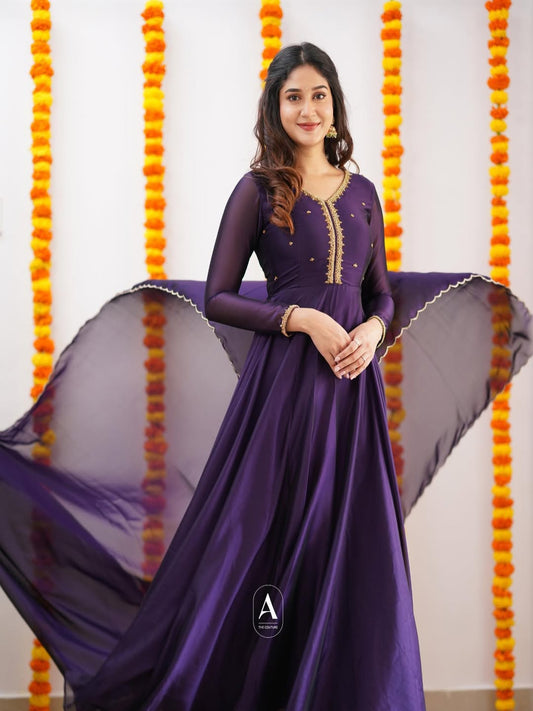 Woman in a purple dress standing against a decorated background with orange and yellow flowers.