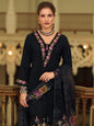 Woman wearing a black embroidered outfit with floral patterns in an elegant indoor setting.