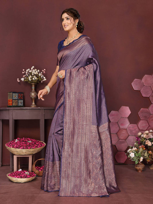 Woman in a purple saree standing in a decorated room with flowers and decor items.