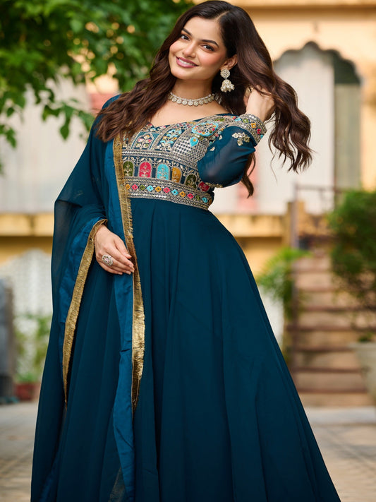 Woman in a traditional blue outfit with intricate designs, standing outdoors.