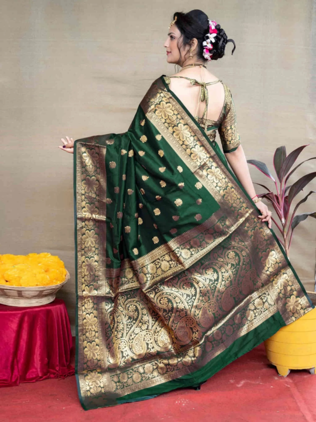 Woman wearing a green saree with gold patterns, standing against a neutral background.