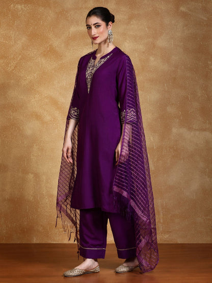 Woman wearing a purple traditional outfit with gold embroidery against a brown background