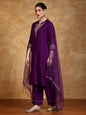 Woman wearing a purple traditional outfit with gold embroidery against a brown background