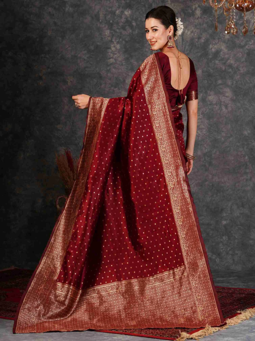 Woman wearing a traditional maroon saree with gold patterns against a dark background