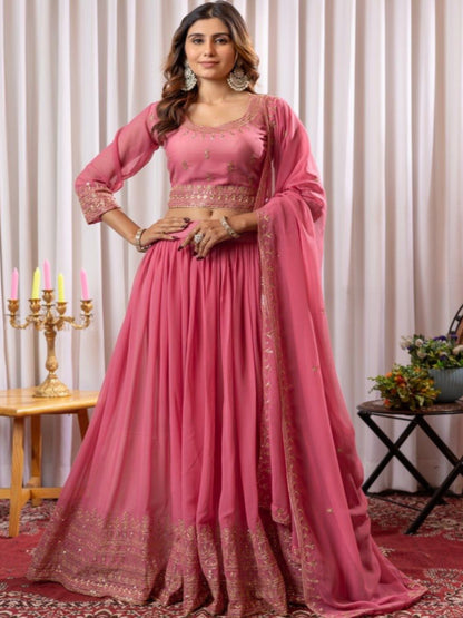 Woman in a pink traditional outfit standing in a decorated room with curtains and decorative items.