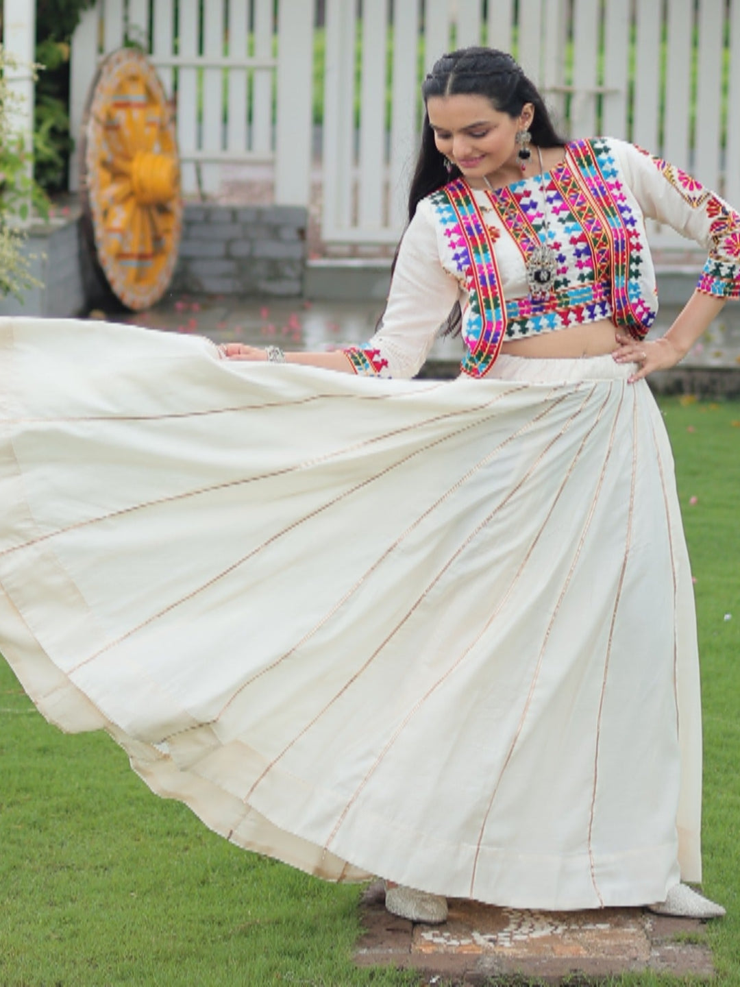 Woman in traditional outfit with colorful blouse and white saree in a garden setting