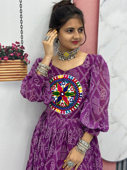 Woman wearing a purple dress with colorful design, standing against a white wall with pink and wooden elements.