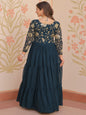 Woman wearing a dark blue traditional outfit with floral patterns in a decorated room.