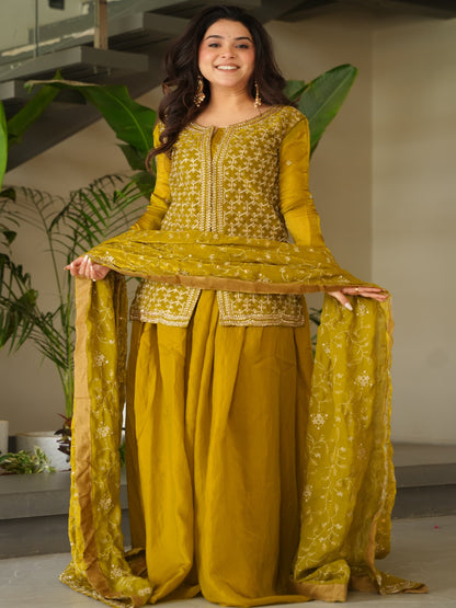 Woman in a yellow traditional outfit standing indoors with plants in the background