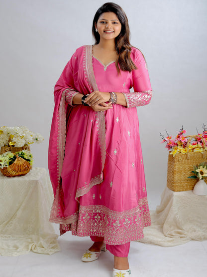 Woman in a pink traditional outfit standing between two floral arrangements on a white background