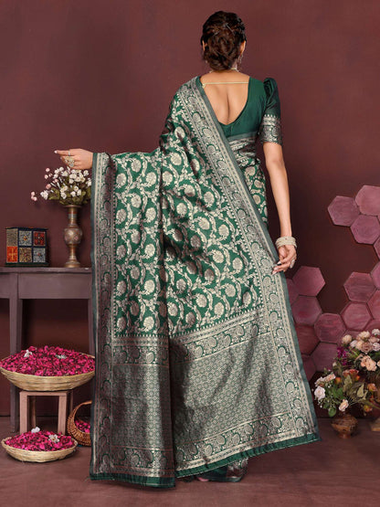 Woman wearing a green saree with a pattern, standing against a brown background with decorative elements.