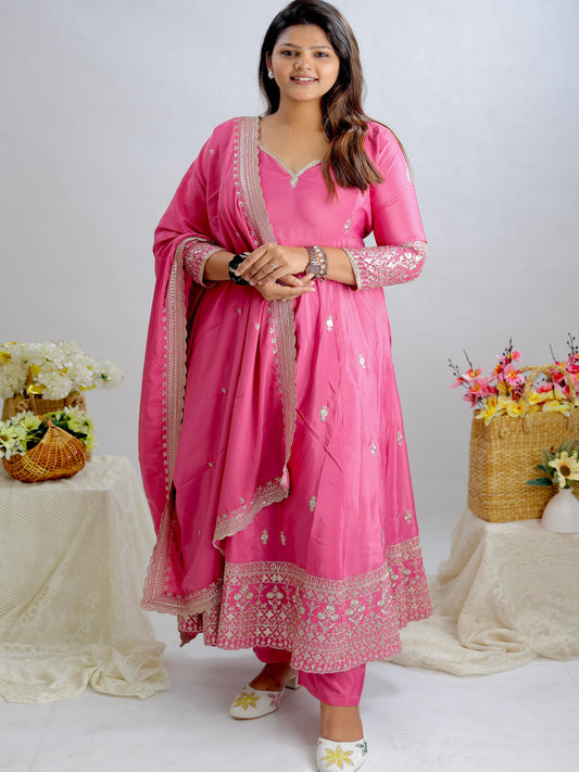 Woman in a pink traditional outfit standing between two tables with floral arrangements.