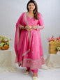 Woman in a pink traditional outfit standing between two tables with floral arrangements.
