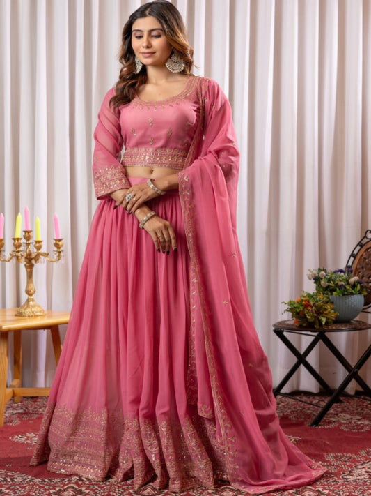 Woman in a pink traditional outfit standing in a decorated room with curtains and a table.
