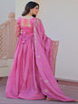 Woman in a pink traditional outfit with a matching dupatta, standing indoors.