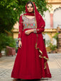 Woman in a red traditional outfit with intricate patterns standing outdoors.
