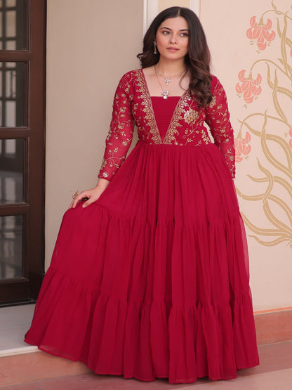 Woman wearing a red traditional outfit with intricate designs in a decorated room.