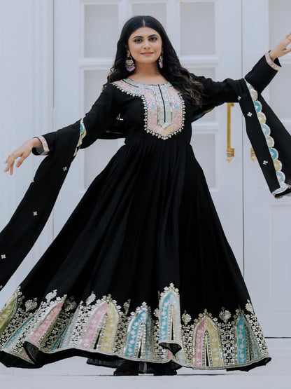 Woman wearing a black embroidered dress with long sleeves against a white door background