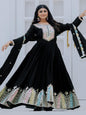 Woman wearing a black embroidered dress with long sleeves against a white door background