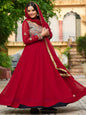 Woman in a red traditional outfit standing outdoors with greenery and architectural elements in the background
