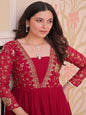 Woman wearing a red embroidered dress with gold details against a decorative wall.