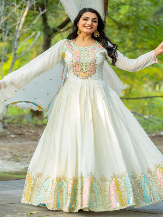 Woman in a white traditional outfit with colorful embroidery standing outdoors.