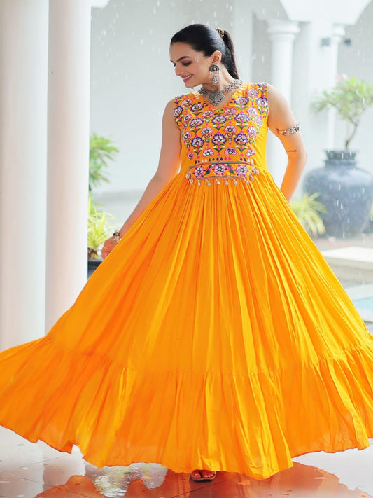 Woman wearing a bright orange traditional gown with intricate patterns in a well-lit room.