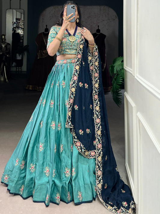 Person wearing a traditional outfit with a teal and navy blue color scheme, standing in a room.